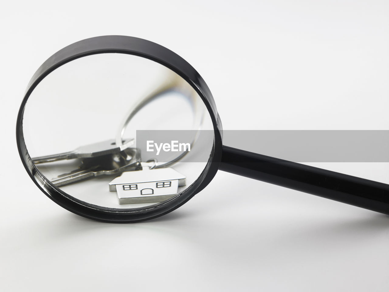 Close-up of house keys seen through magnifying glass on white background