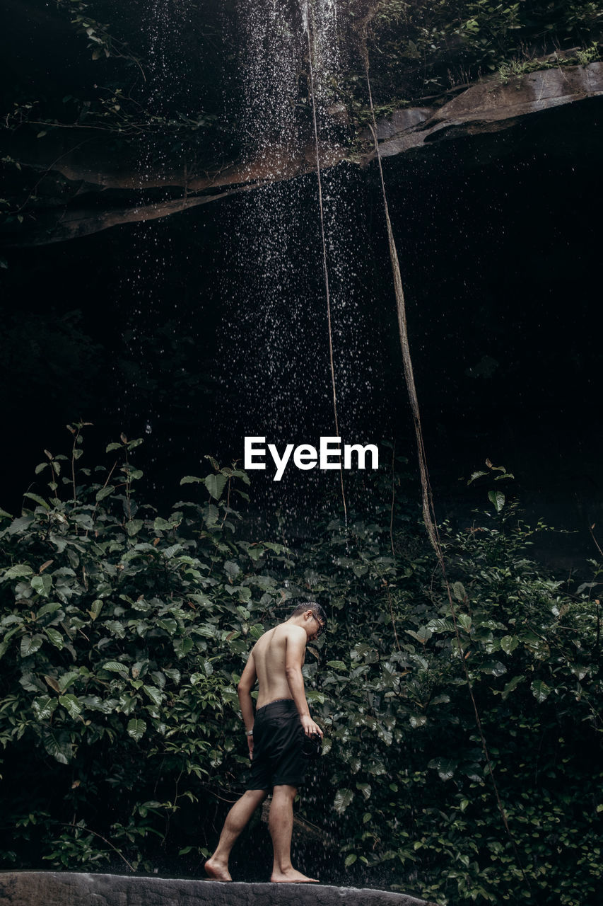 Full length of shirtless man standing at waterfall