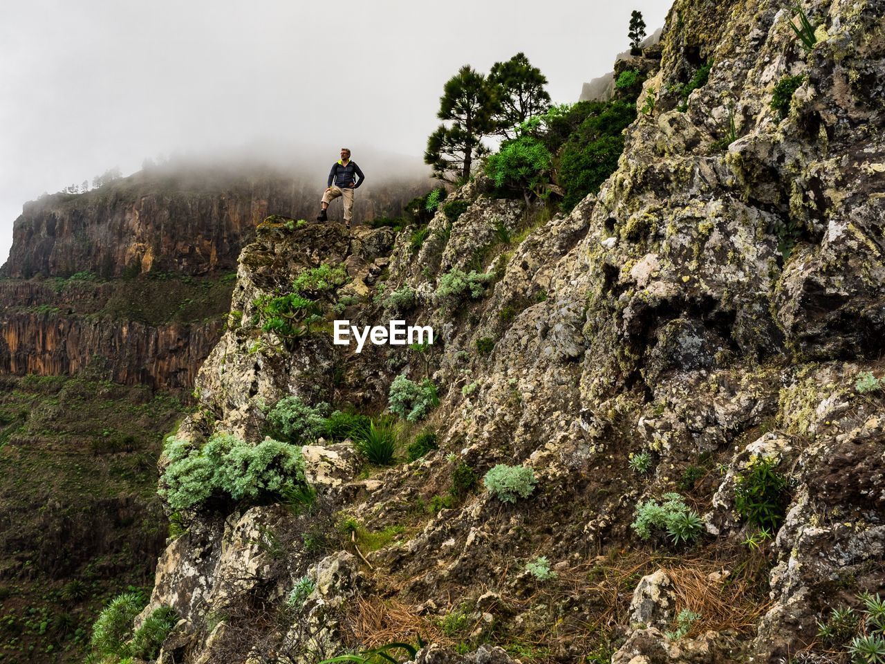 Low angle view of man standing on cliff against sky