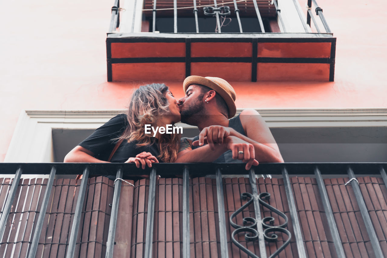 Low angle view of young couple kissing at balcony