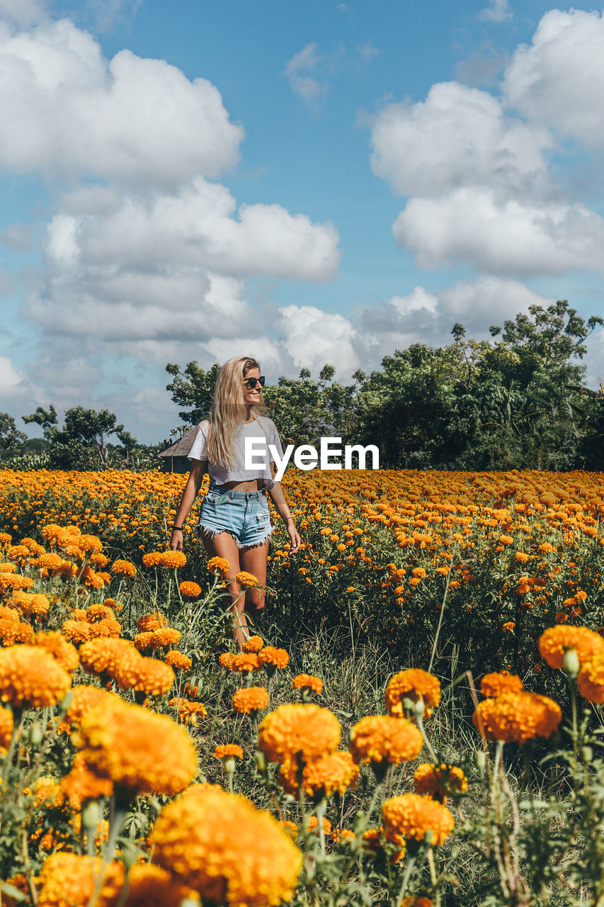 Woman standing amidst yellow flowers on field against sky