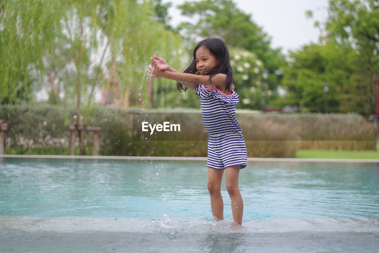 Portrait of a cute asian girl standing in the pool on a clear day. happily