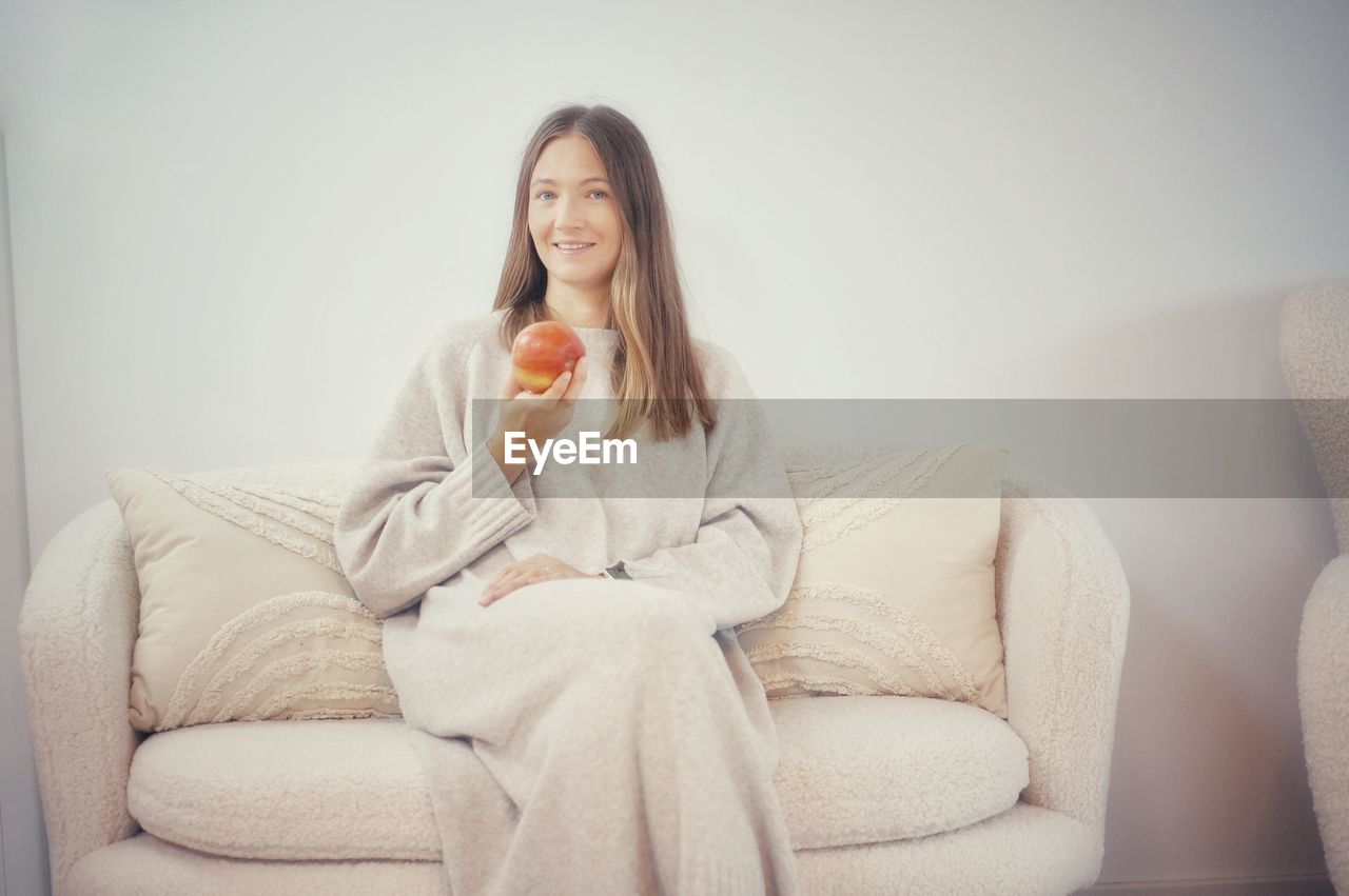 portrait of young woman using phone while sitting on sofa at home