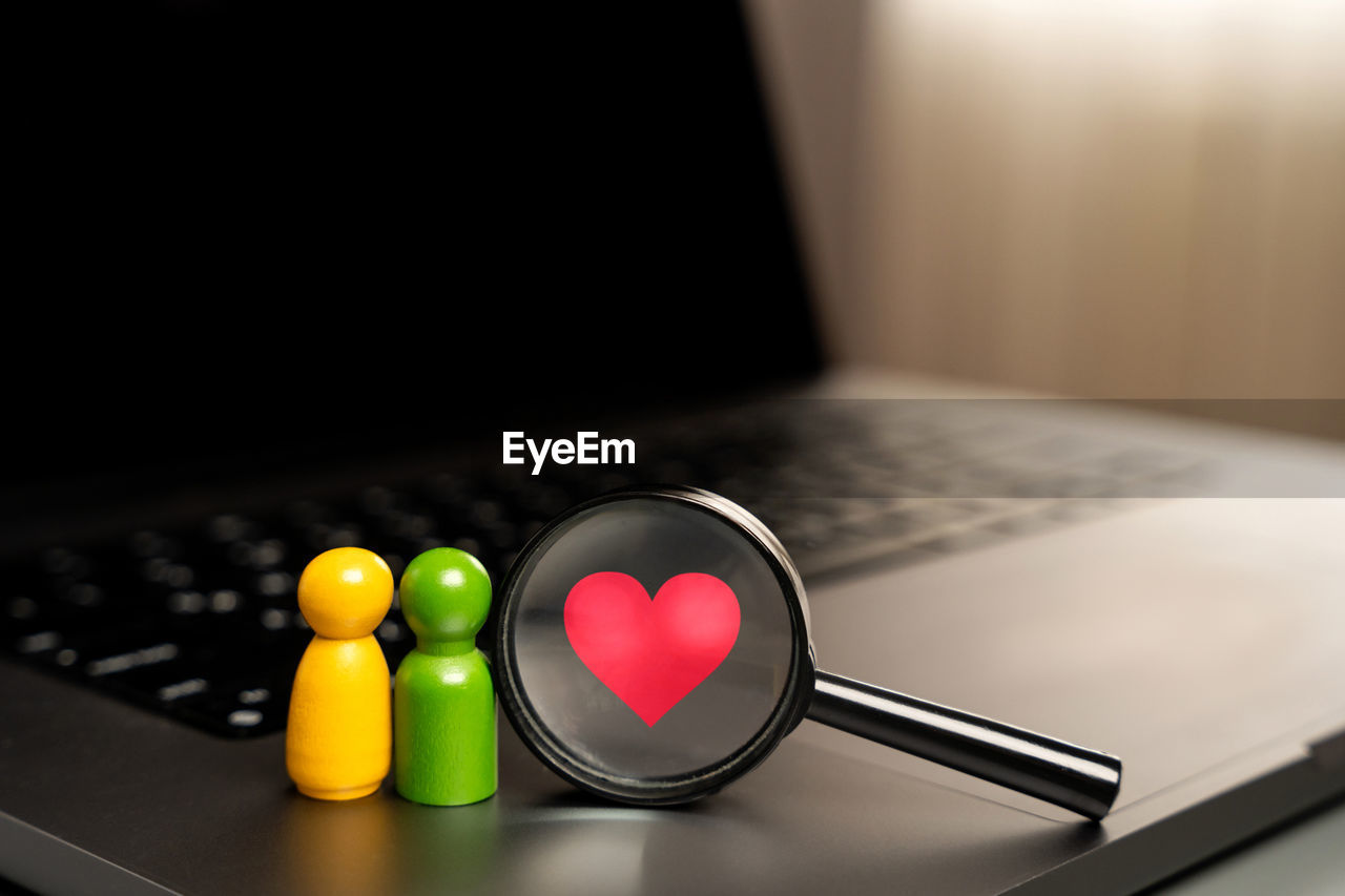 A figurine of people in the form of a pair of lovers stands on the keyboard near a magnifying glass. 