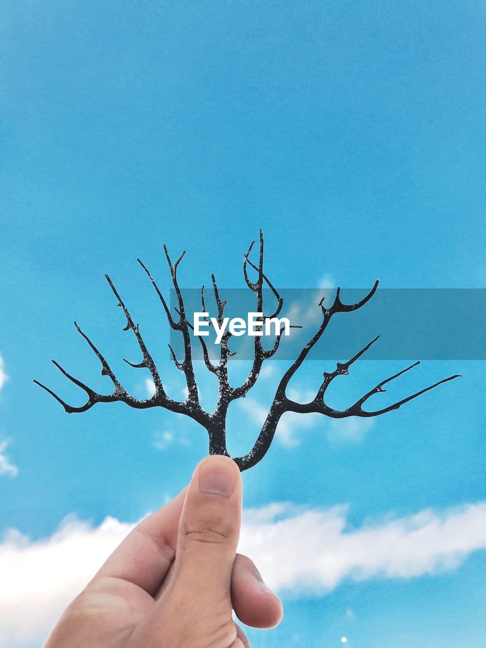 Cropped hand holding artwork against blue sky