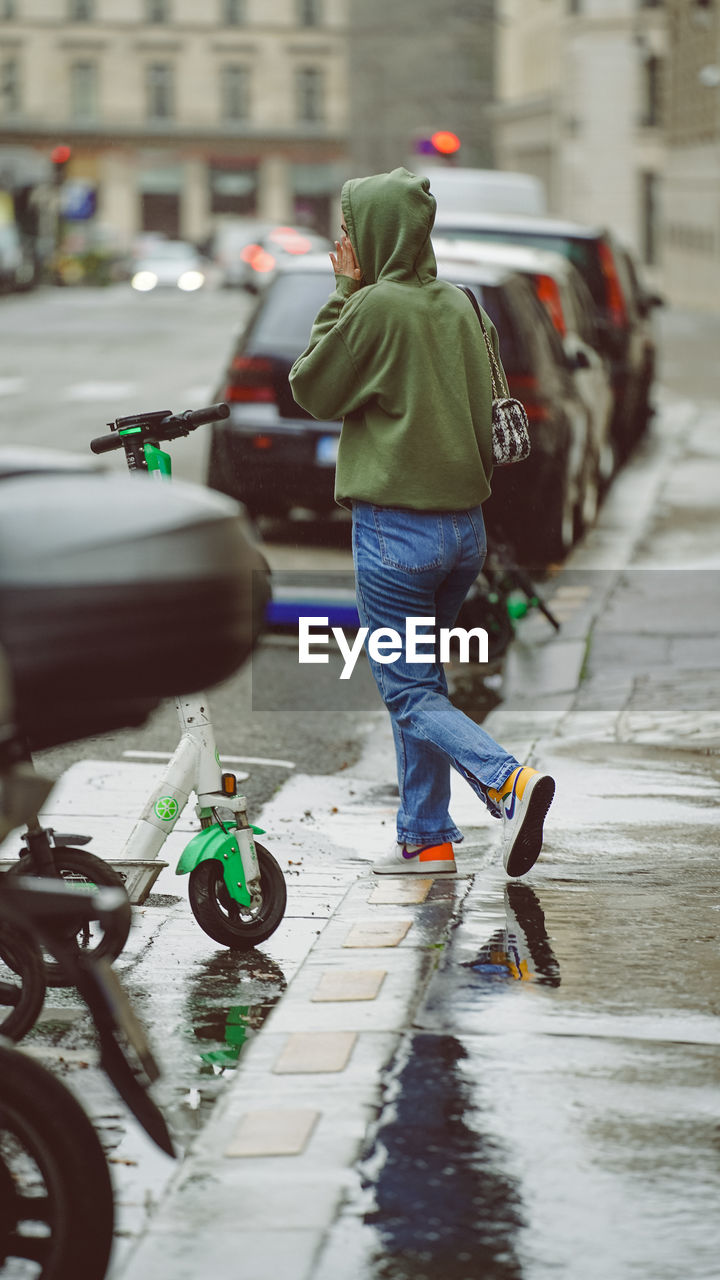 REAR VIEW OF MAN ON WET STREET