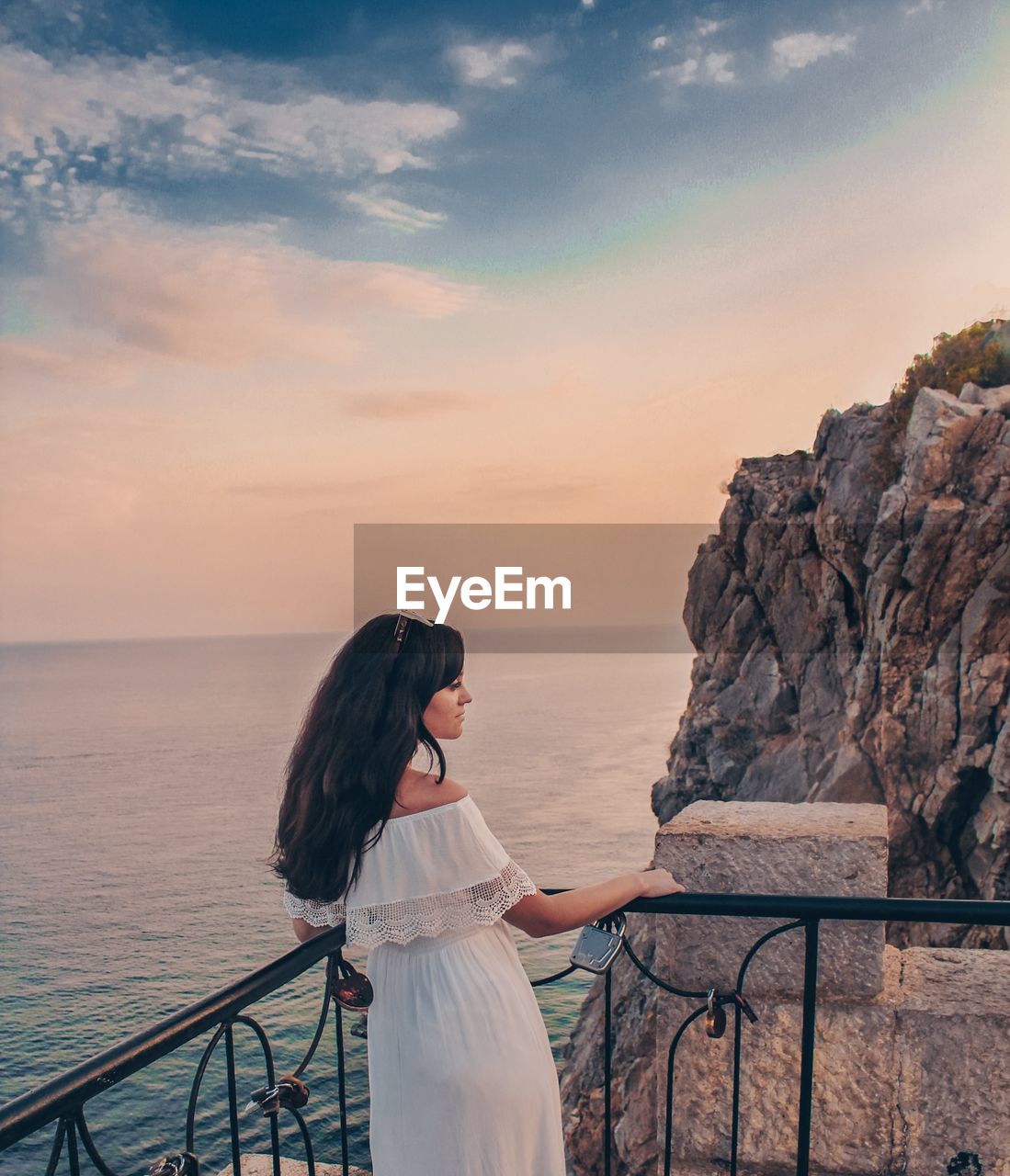 Young woman standing by railing against sea during sunset