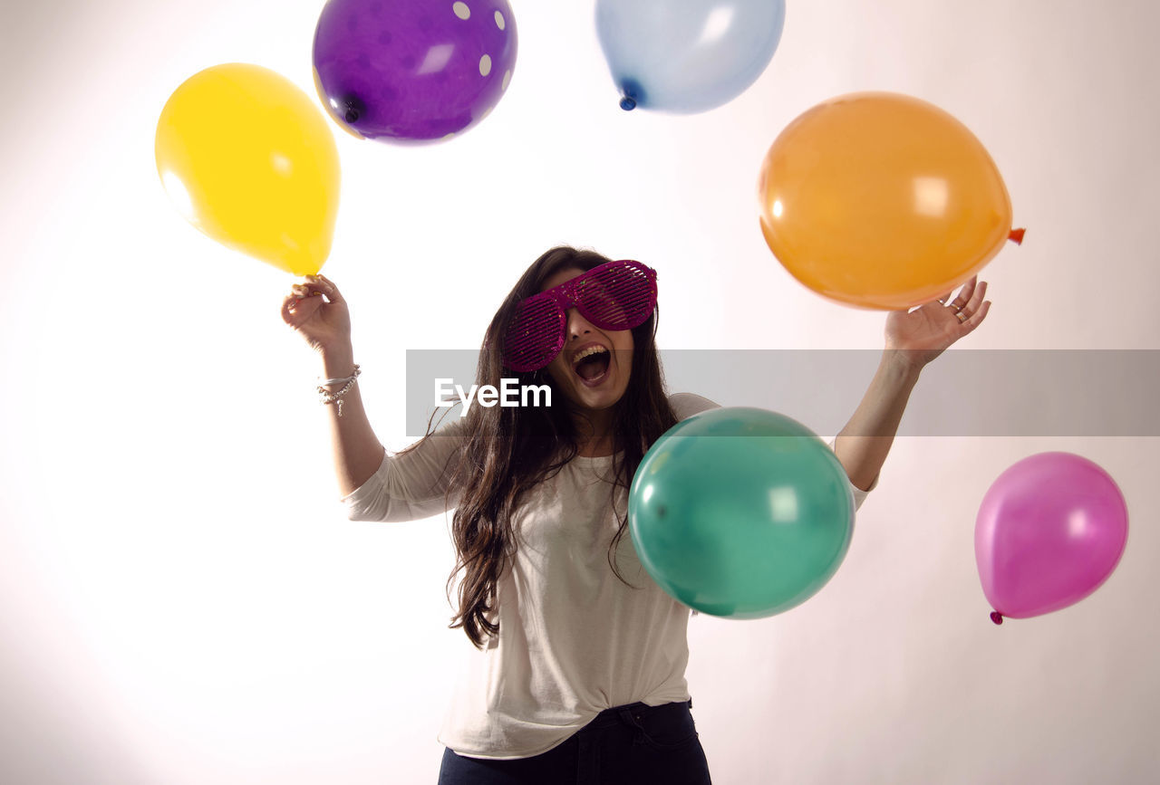 Happy young woman playing with colorful balloons against wall