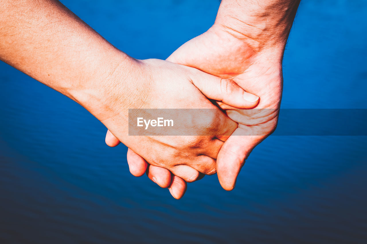 Cropped hand of man and woman against river