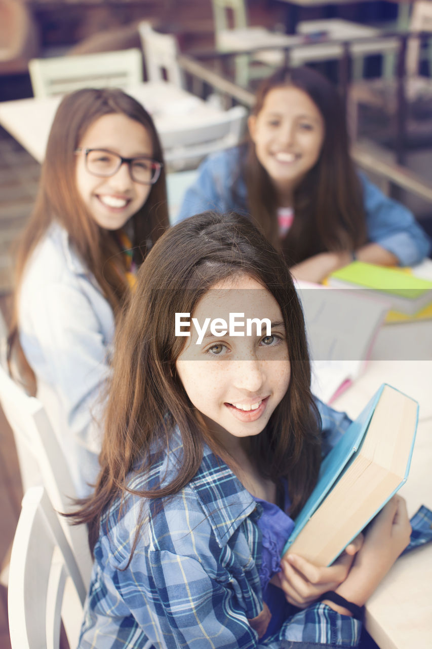 Portrait of smiling teenage friends with books sitting on desk