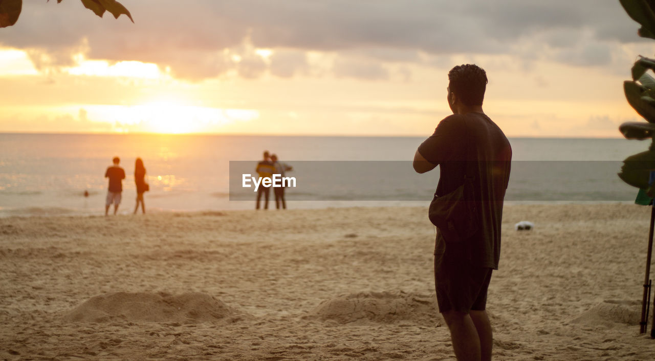 Rear view of man on beach against sky during sunset