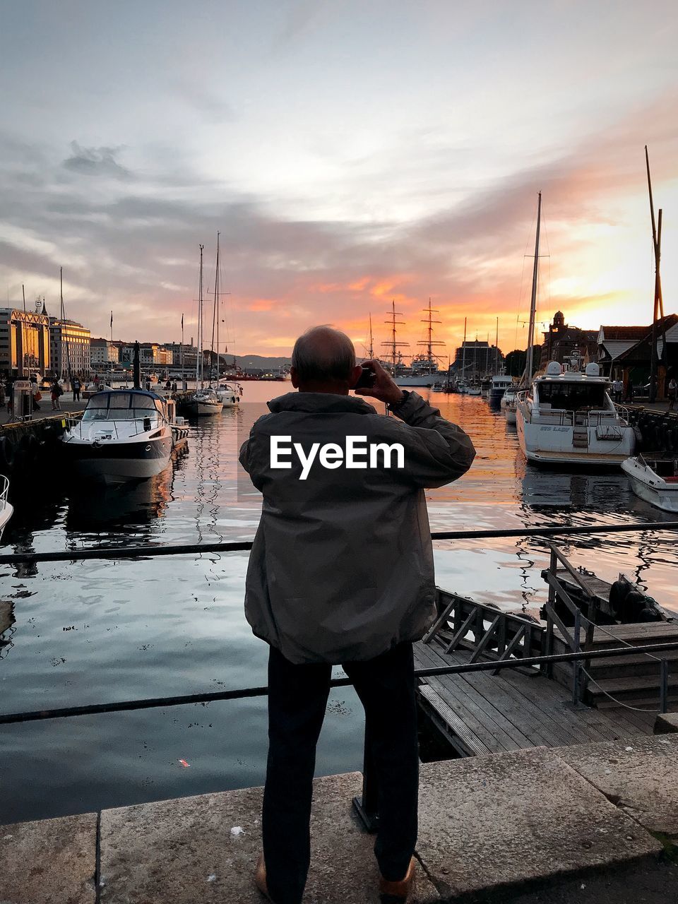 Rear view of man standing at harbor during sunset