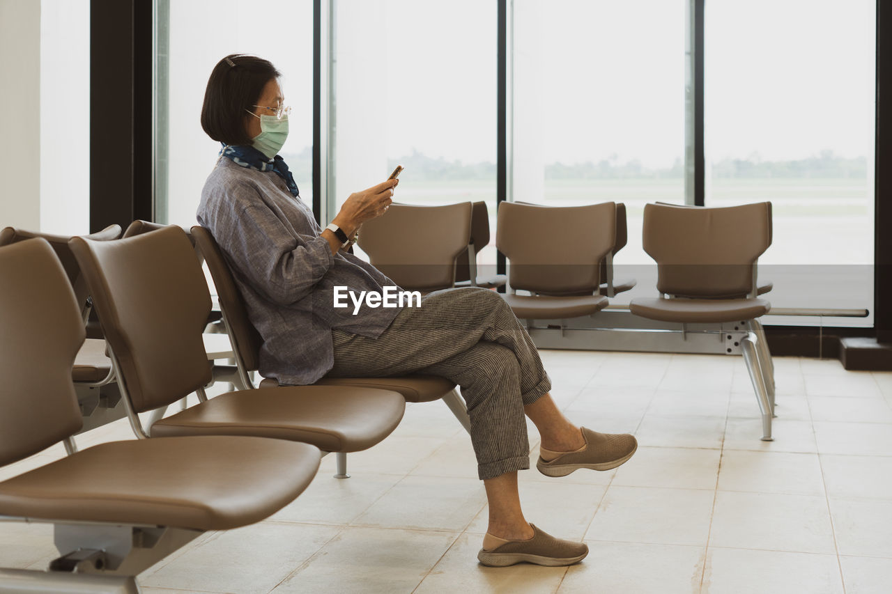 SIDE VIEW OF WOMAN SITTING ON CHAIR IN FRONT OF BUILDING