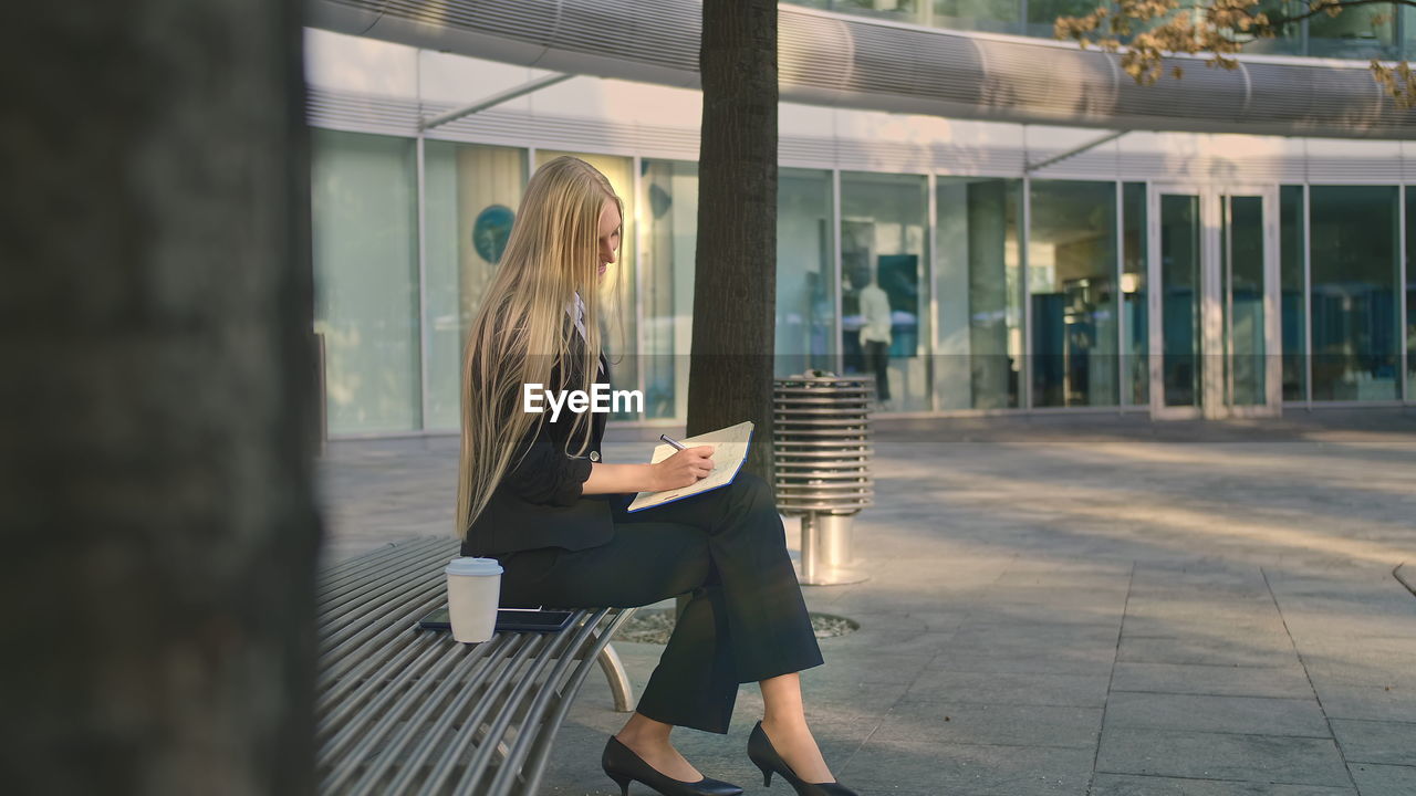 Businesswoman holding digital tablet sitting on bench outdoors