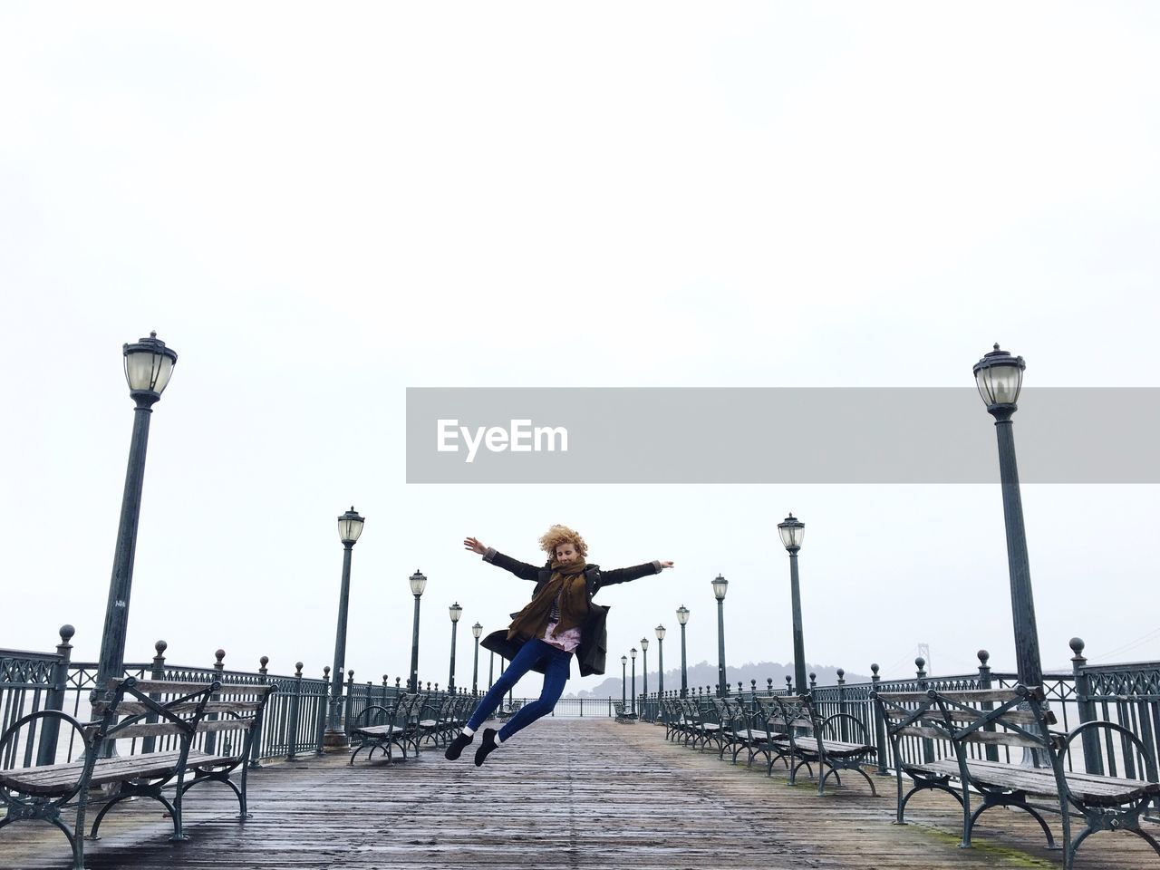 Young woman jumping on pier against clear sky