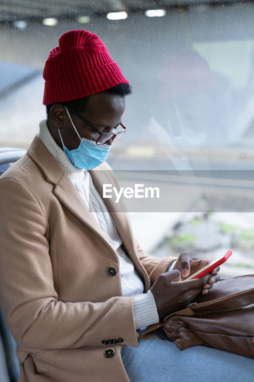 Young man wearing mask using smart phone sitting in bus