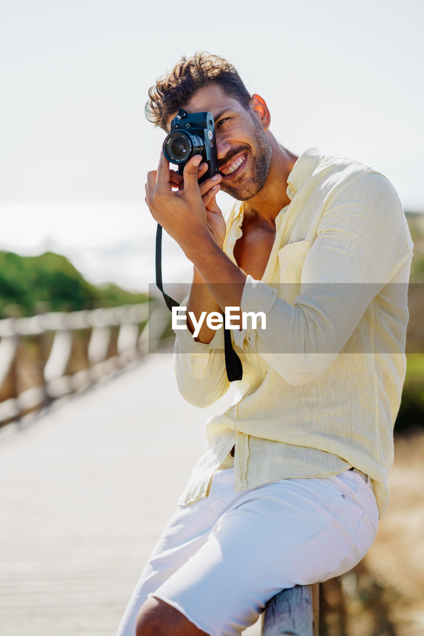 Smiling man with camera photographing while standing by railing