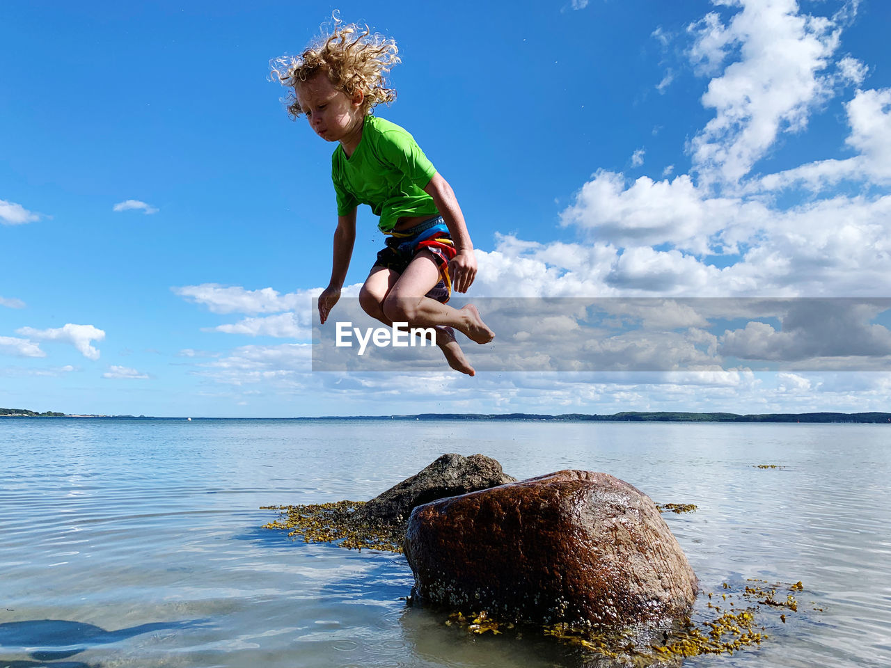 Boy jumping on rock in sea against sky