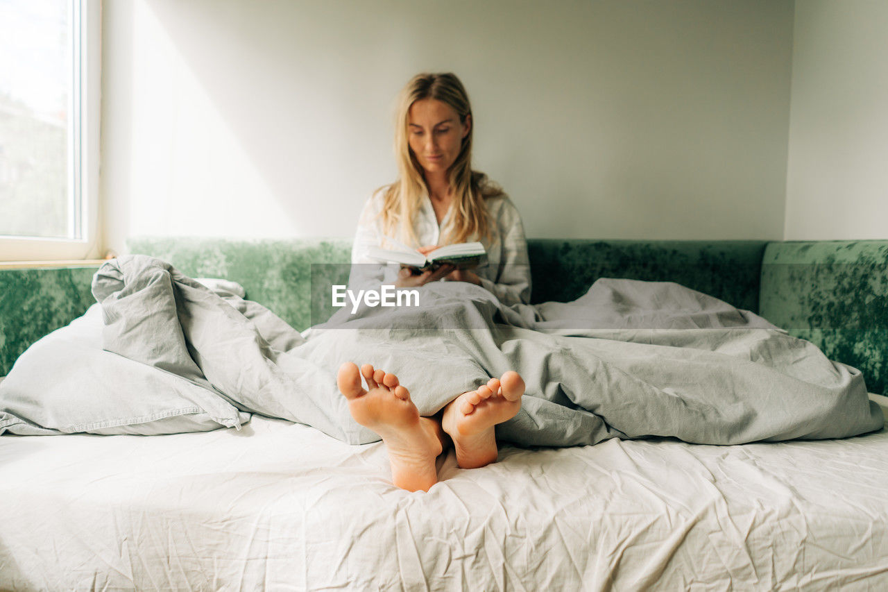 A woman is reading while sitting in bed. blurred portrait of a woman, focus on the feet. person