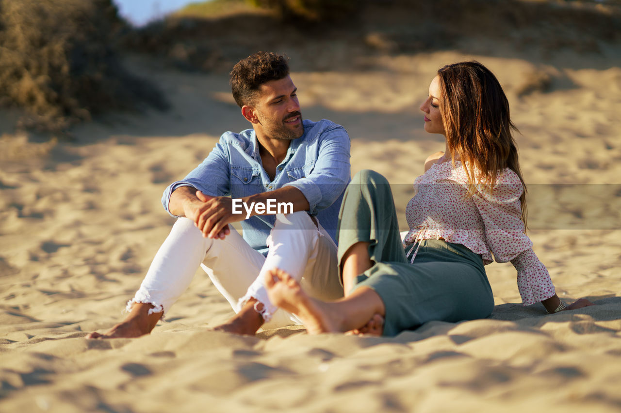 Couple talking while sitting on sand at beach