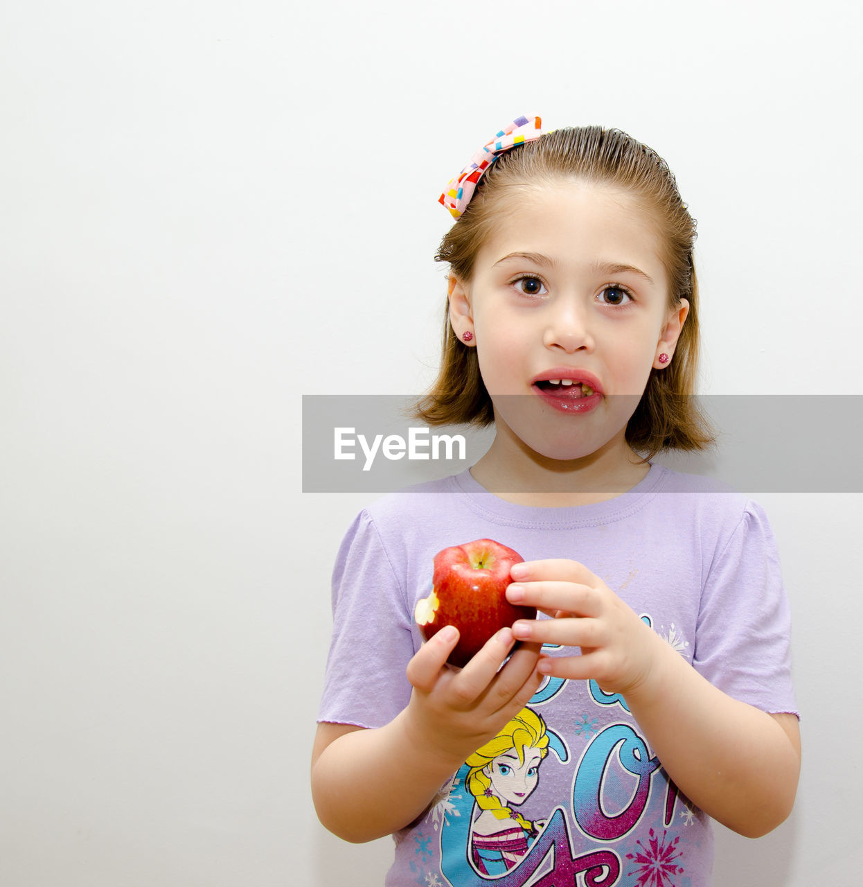 Portrait of girl eating apple against white background