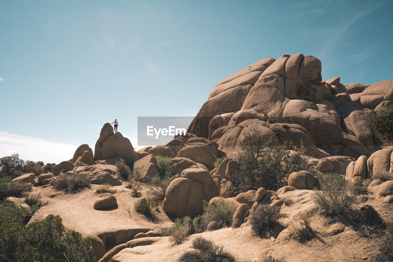 Woman climbing rock surreal formation against blue sky