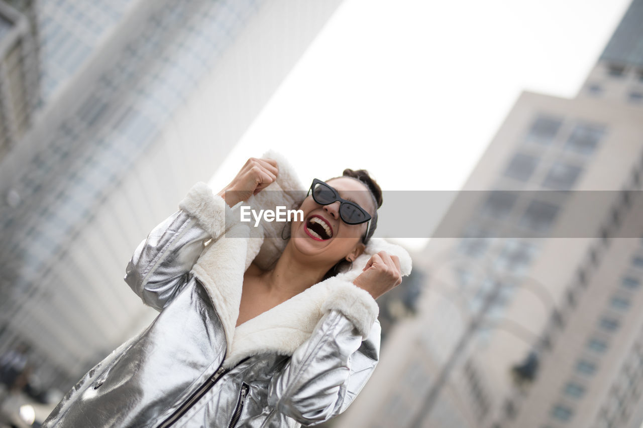 Laughing woman in sunglasses against buildings