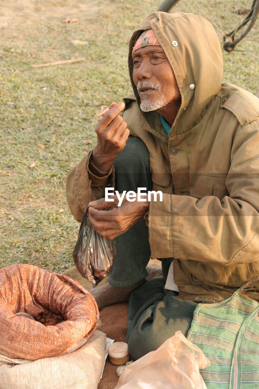 Senior vendor selling food while sitting on grassy field