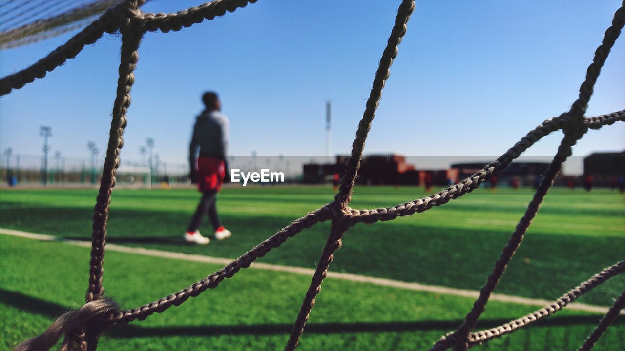 Man seen through fence walking on field against sky