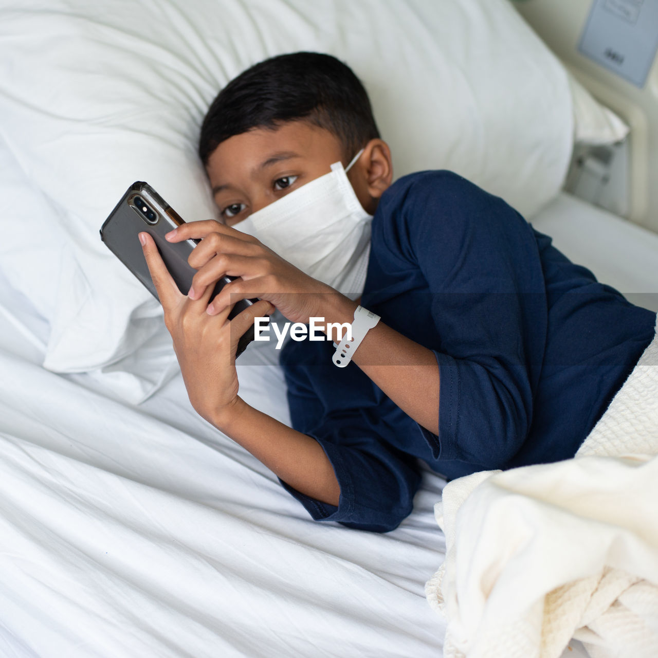 Boy wearing mask using mobile phone at hospital