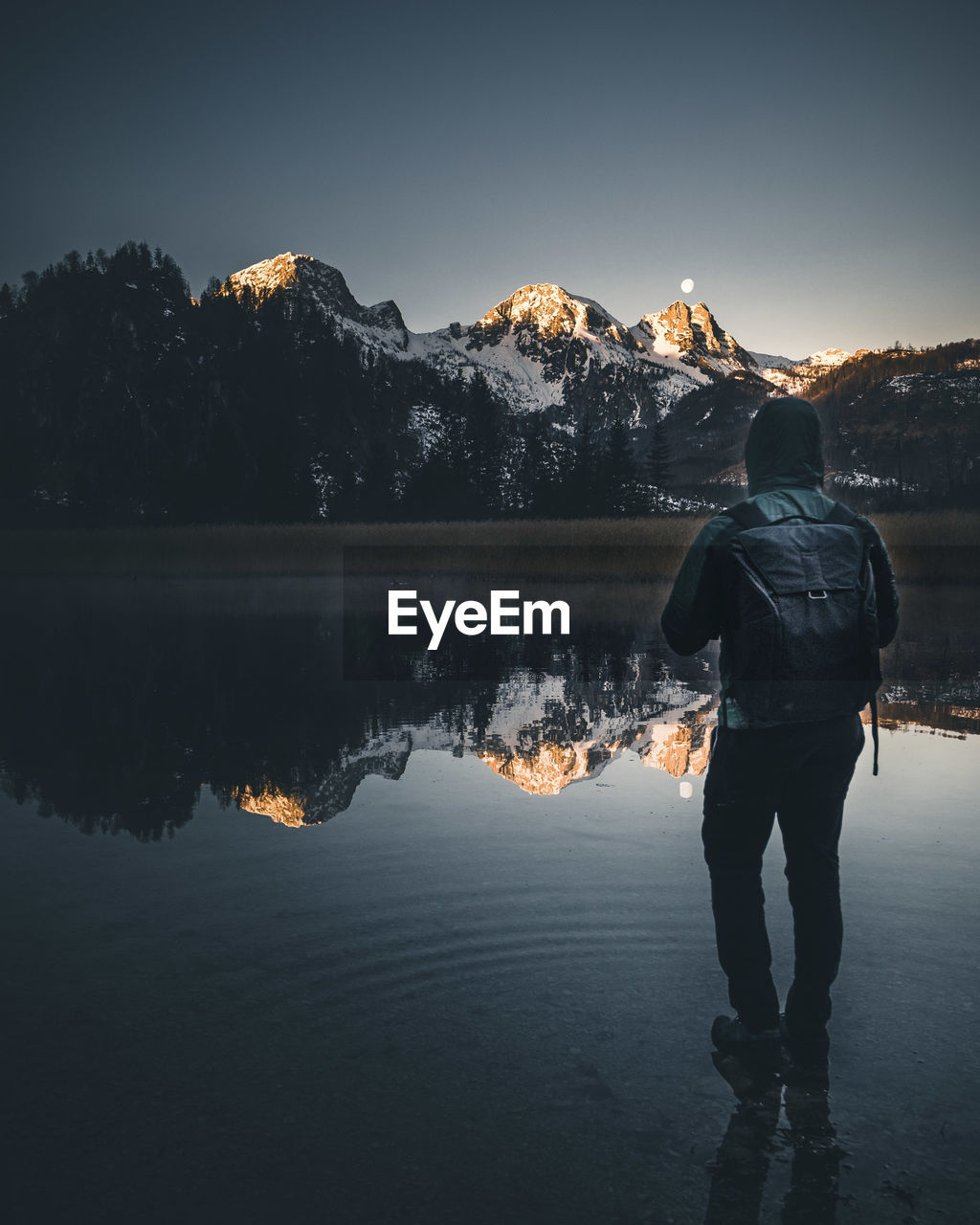 REAR VIEW OF MAN STANDING AT LAKE AGAINST SKY