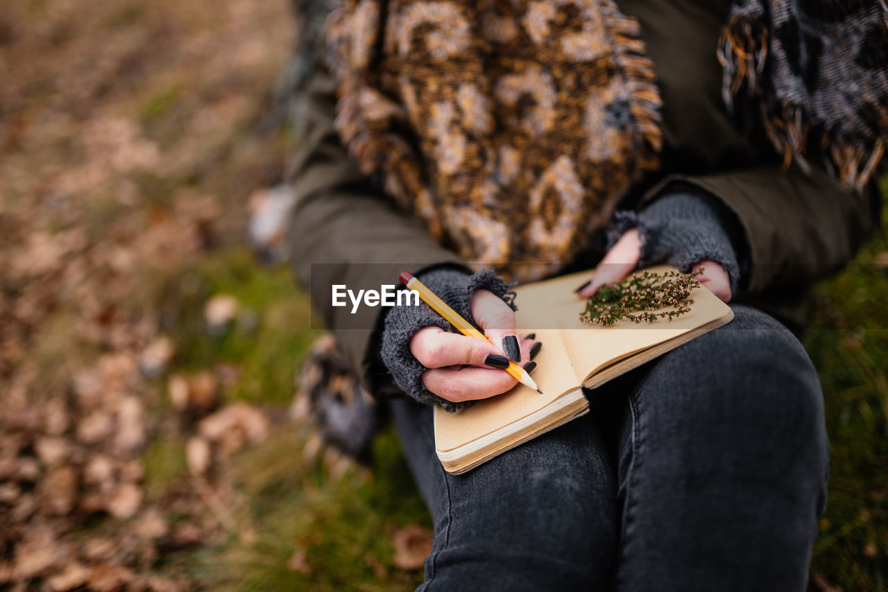 Midsection of woman writing in diary at forest