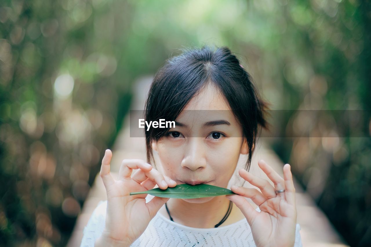 Portrait of young woman holding leaf while standing outdoors