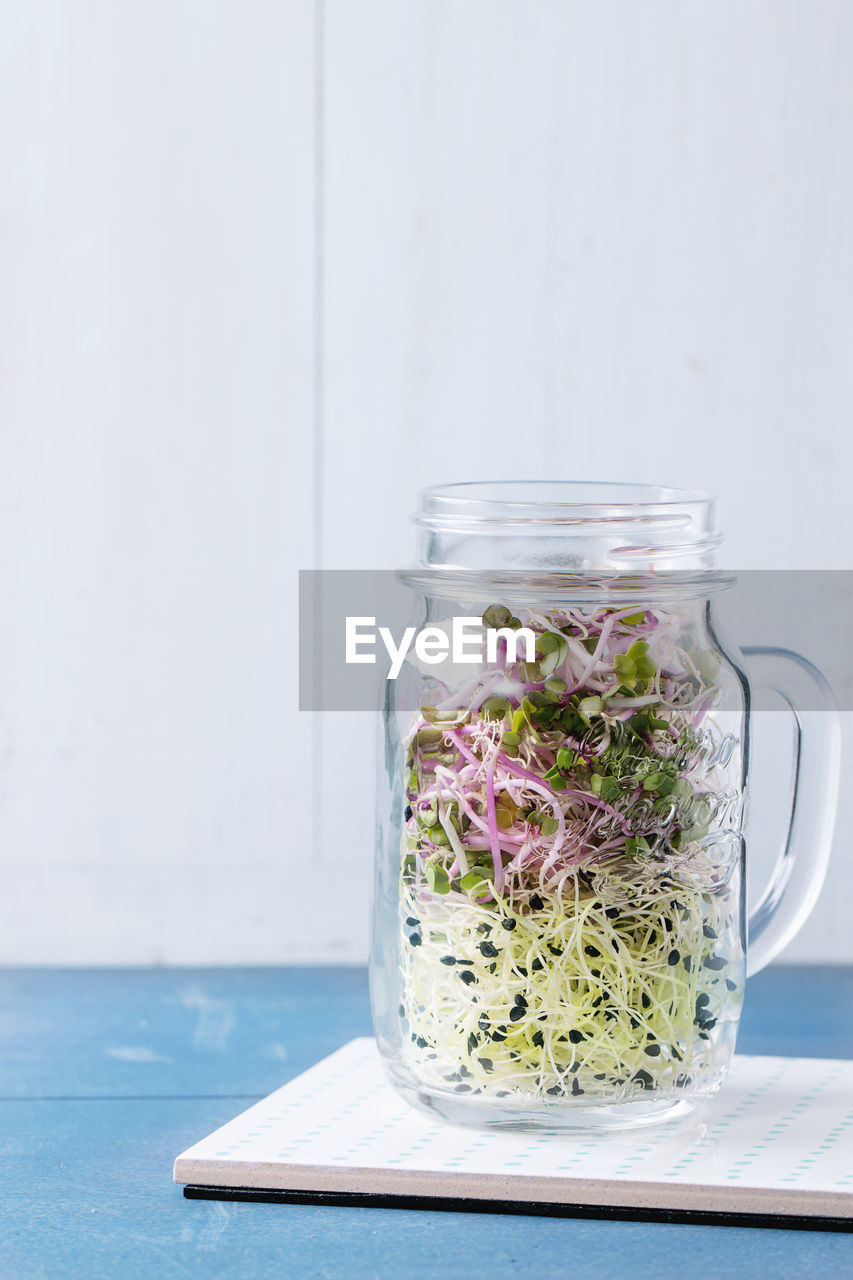 Close-up of bean sprouts in jar on table against wall