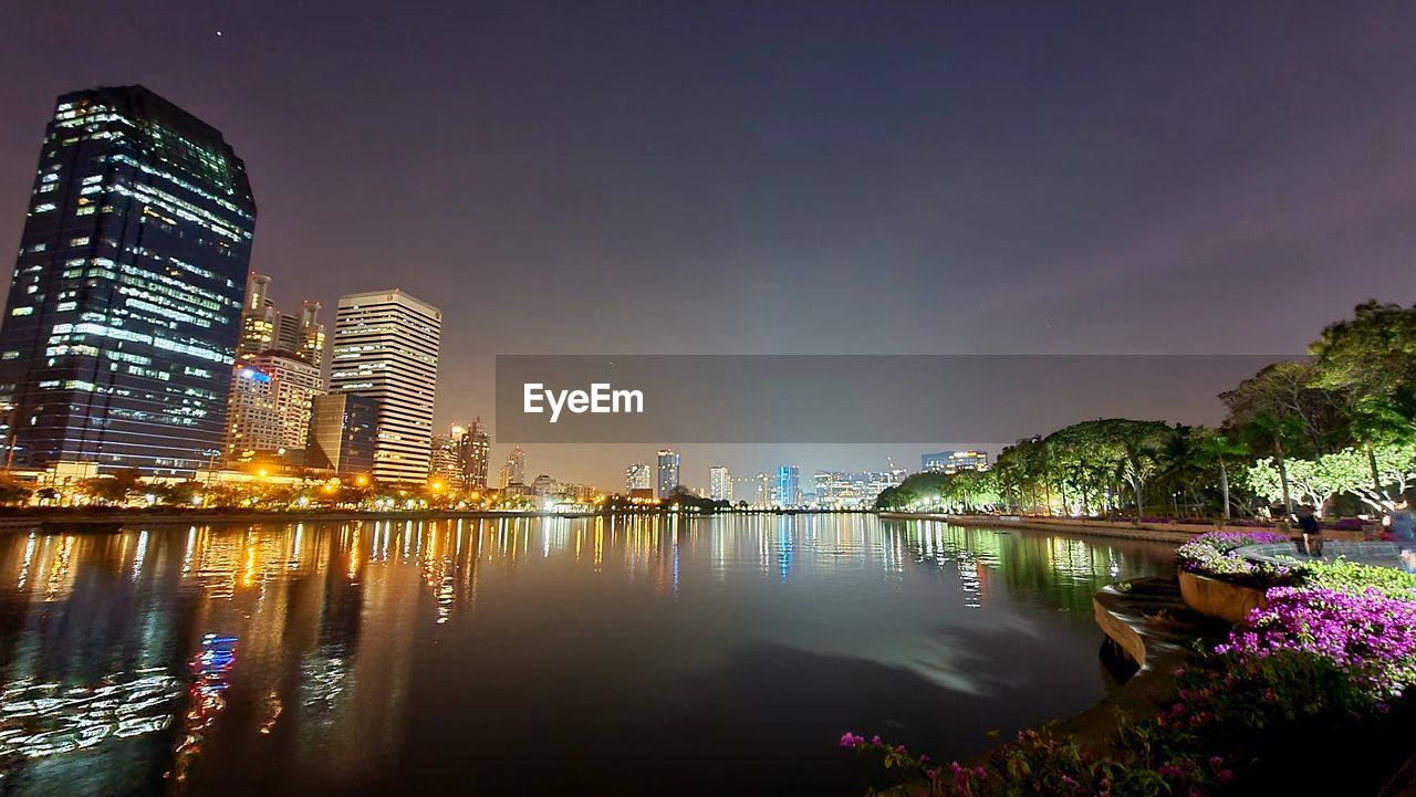 ILLUMINATED BUILDINGS BY RIVER AGAINST SKY