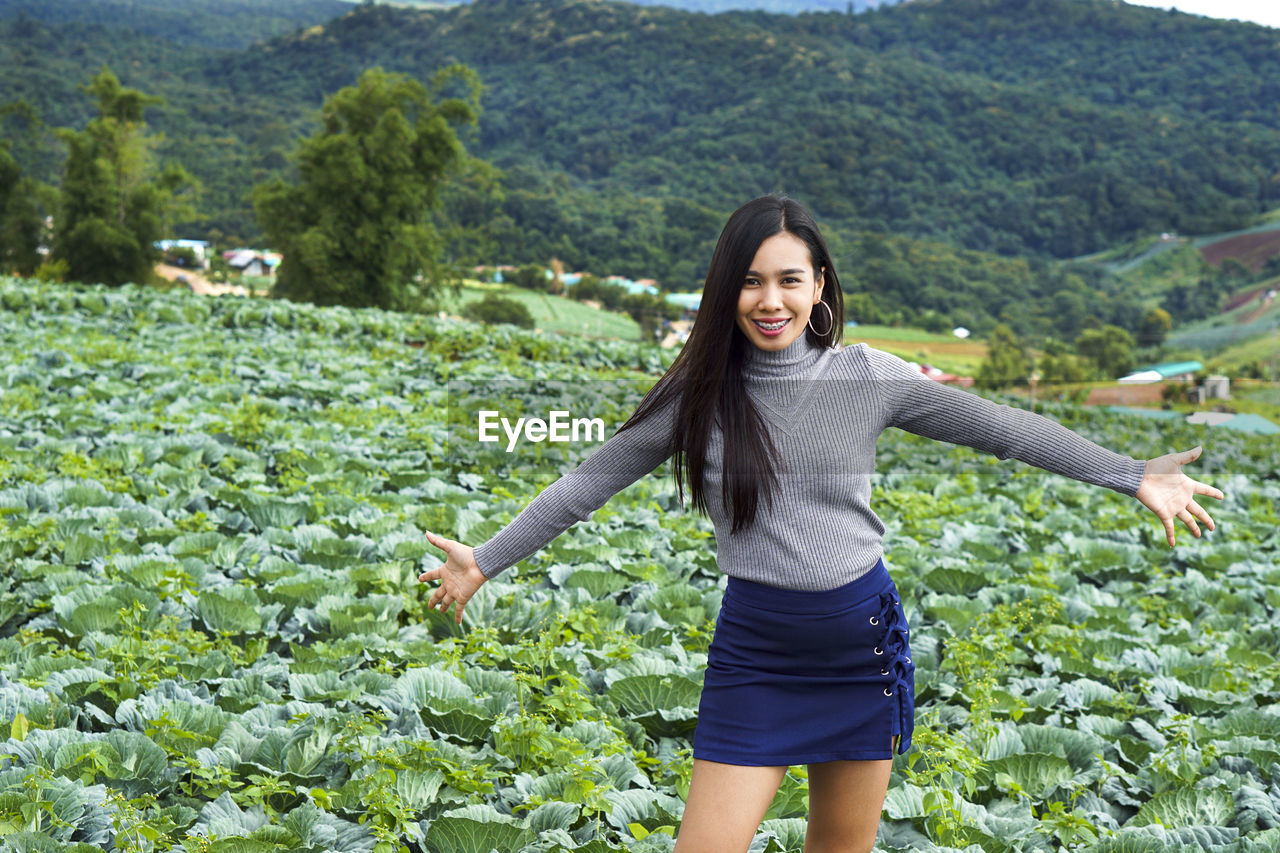 Happy young woman with arms outstretched against trees