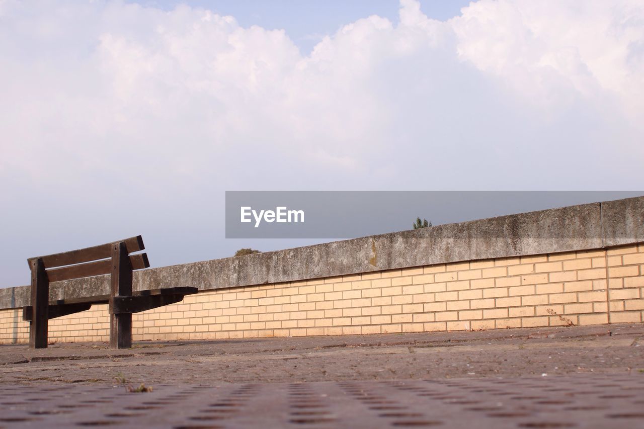 Low angle view of empty bench on promenade against cloudy sky