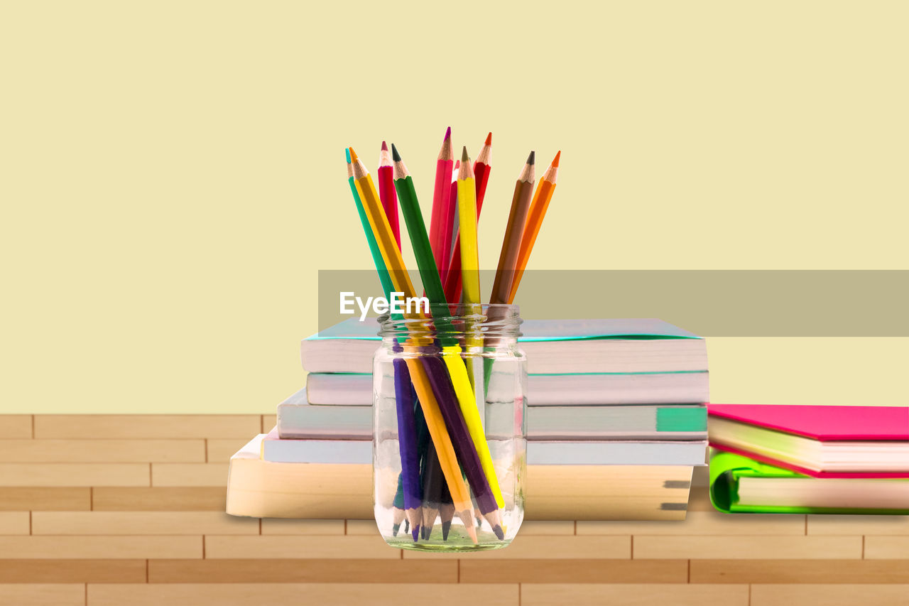 Close-up of multi colored pencils and books on table against beige wall