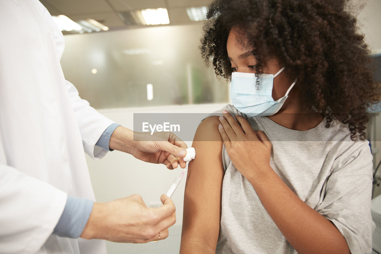 Girl with protective face mask taking covid-19 vaccination at hospital