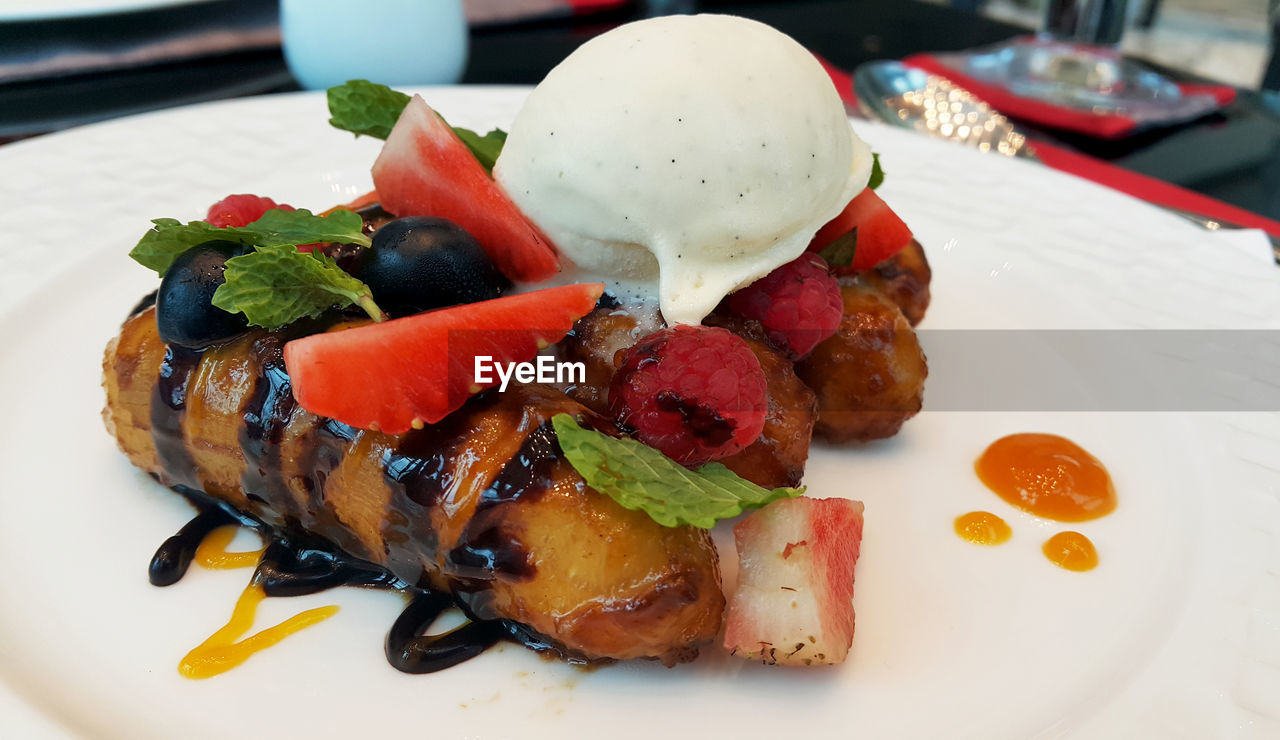 Close-up of fried banana with fruits and ice cream on plate