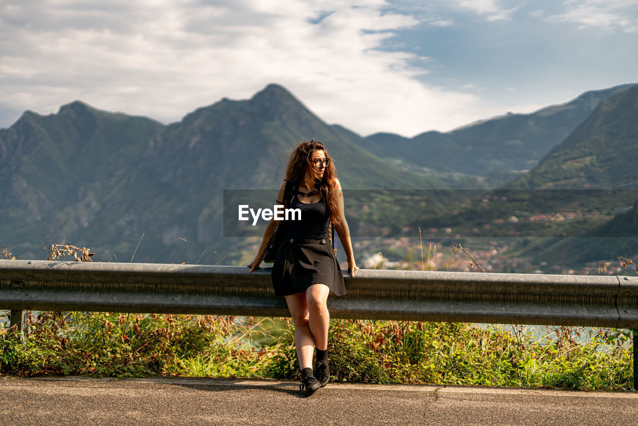 Woman looking away while standing by railing against mountains