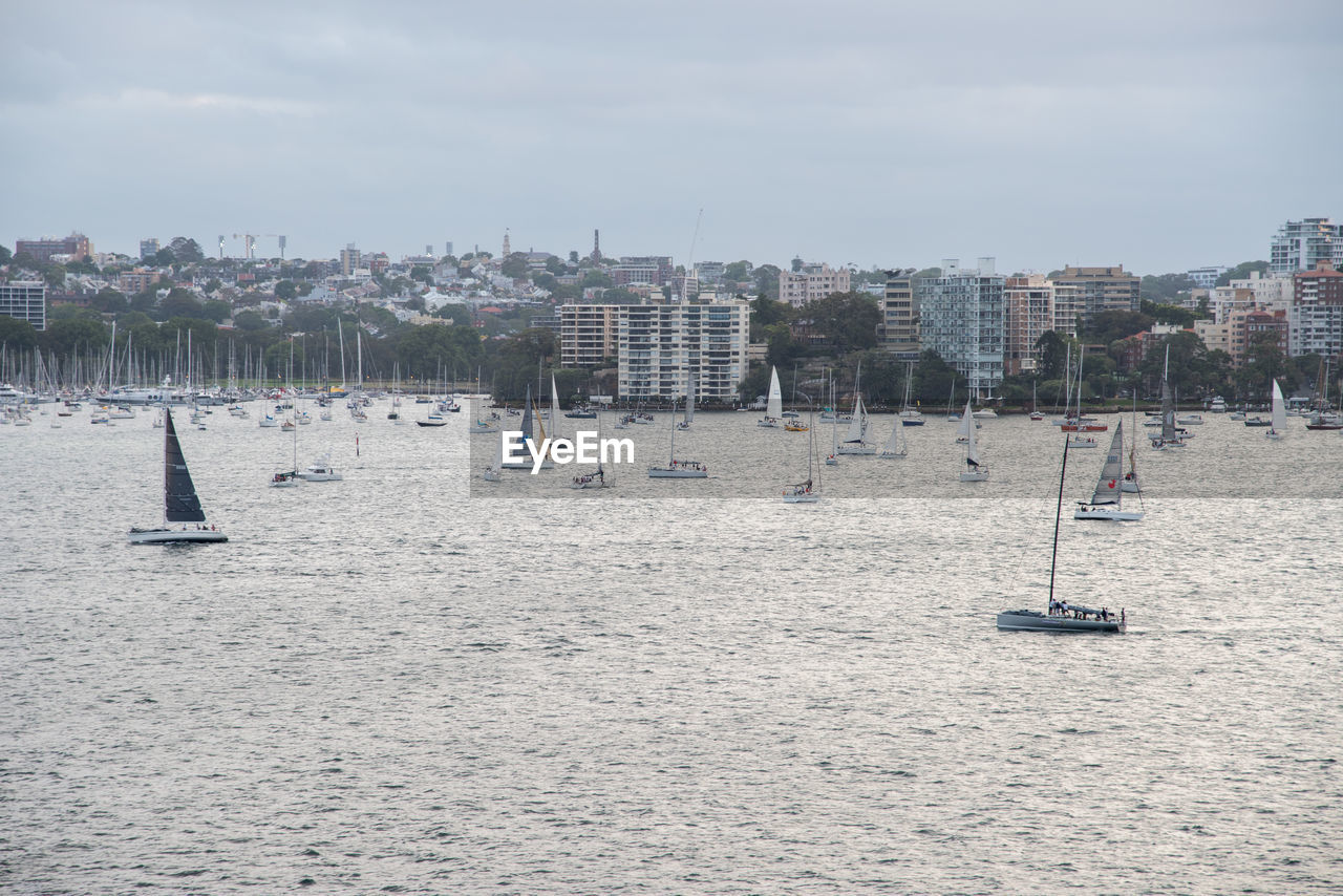 SAILBOATS SAILING ON SEA BY CITY AGAINST SKY