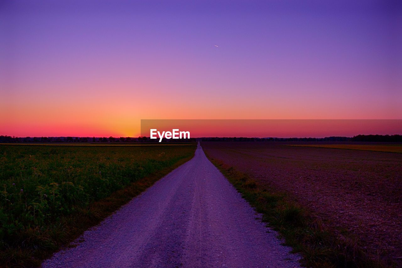 Road amidst field against sky during sunset