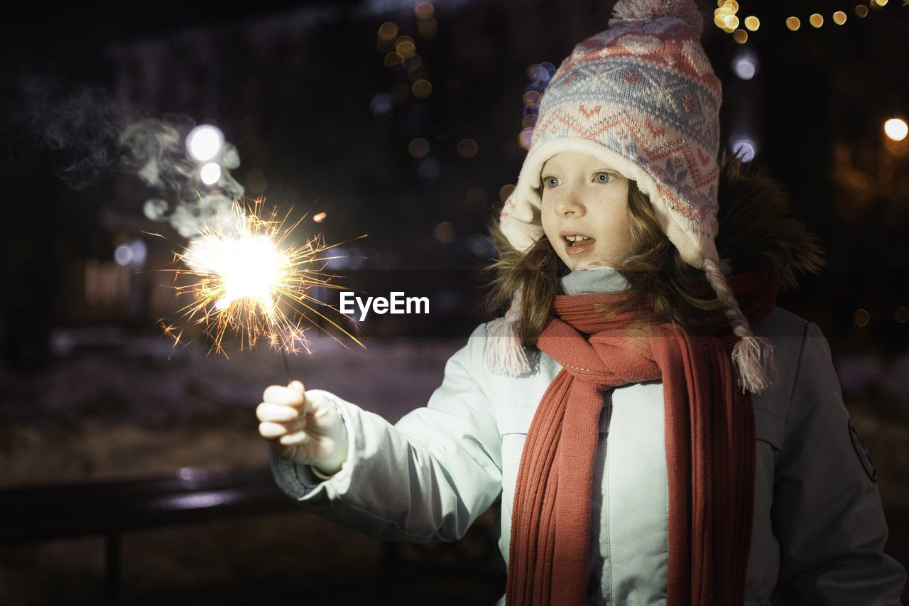 Portrait of young woman holding sparkler at night