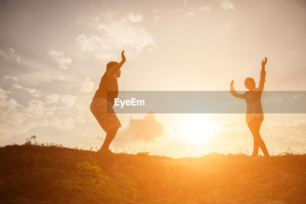 FRIENDS STANDING ON FIELD AGAINST SKY DURING SUNSET