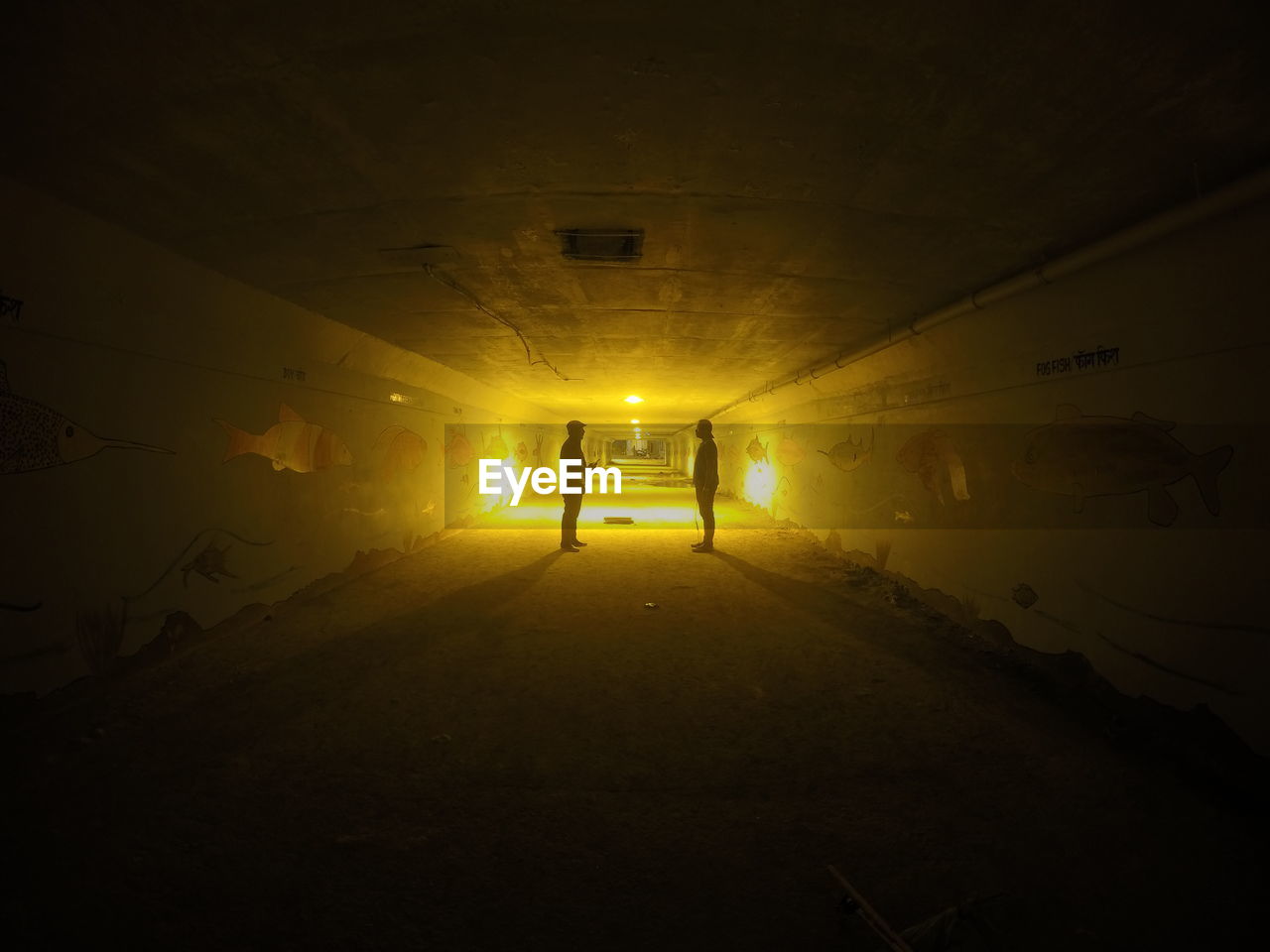 Side view of two silhouette people standing in tunnel