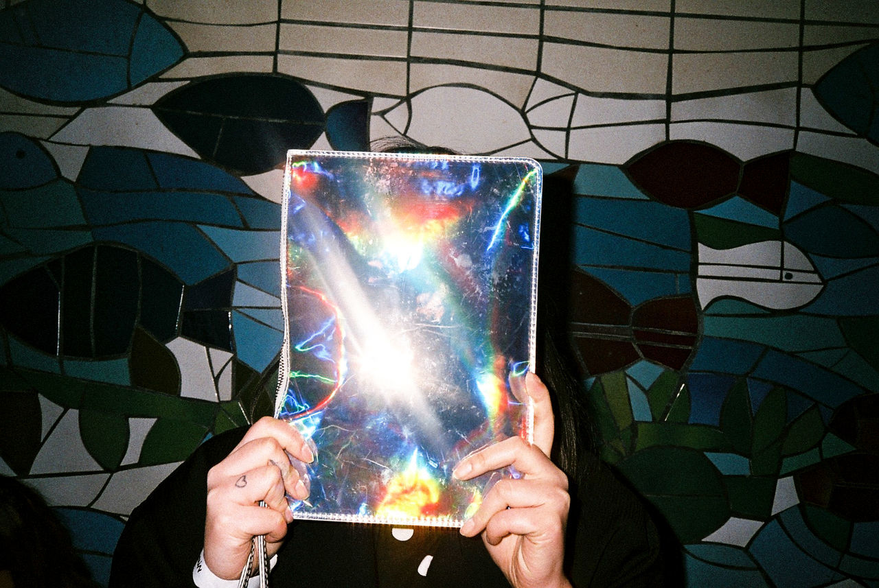 Woman covering face with shiny sheet against wall