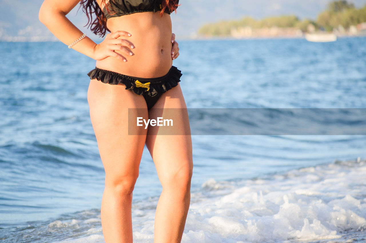 Midsection of sensuous woman wearing bikini standing at beach