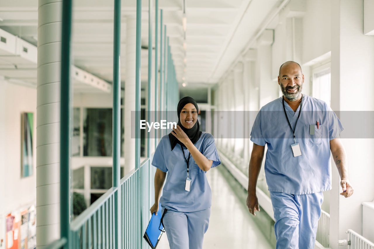 Portrait of coworkers talking while walking in corridor at hospital