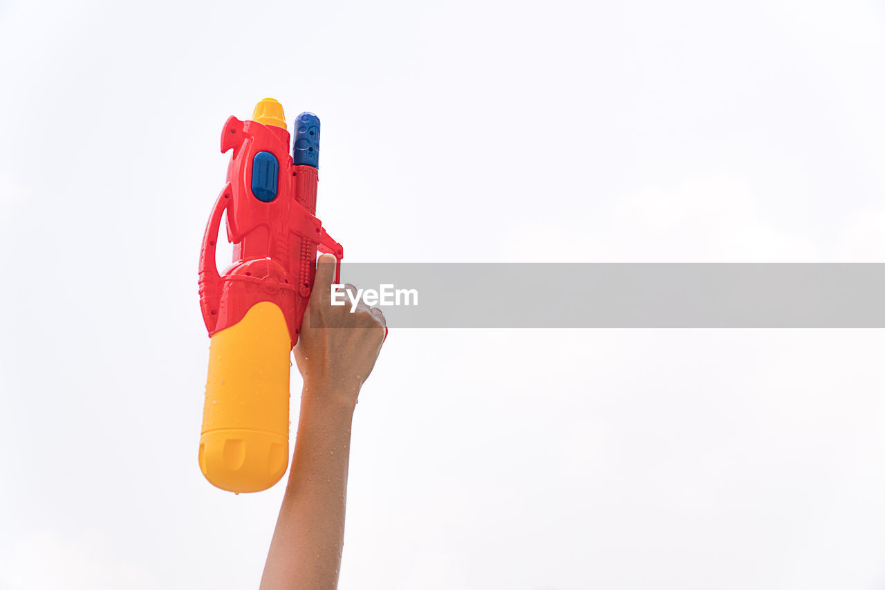 Cropped hand holding squirt gun against white background
